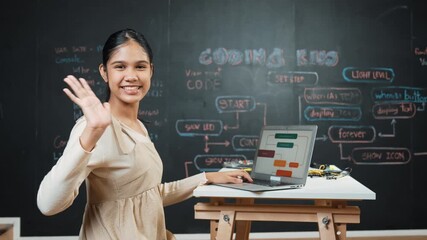 Smart high school girl waving to camera while programming code at blackboard with engineering code or prompt written. Academic student working on laptop or writing program and greeting. Edification