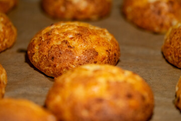 Freshly baked cheese buns cooling on parchment paper. The buns have a golden-brown crust, indicating perfect baking. Ideal for illustrating homemade baking or culinary delights.
