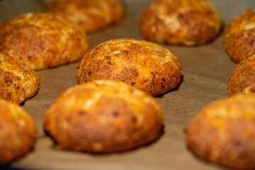 Freshly baked cheese buns cooling on parchment paper. The buns have a golden-brown crust, indicating perfect baking. Ideal for illustrating homemade baking or culinary delights.
