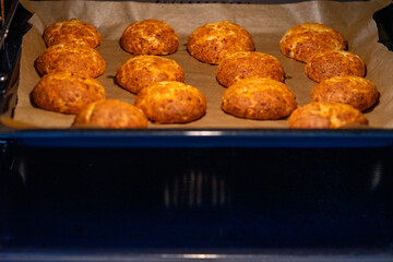 Freshly baked cheese buns cooling on parchment paper. The buns have a golden-brown crust, indicating perfect baking. Ideal for illustrating homemade baking or culinary delights.
