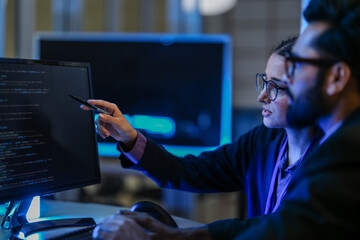 diverse AI developers collaborate in a late-night coding session. A senior engineer mentors his colleague as they program a complex machine learning algorithm together.
