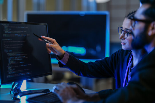 diverse AI developers collaborate in a late-night coding session. A senior engineer mentors his colleague as they program a complex machine learning algorithm together.