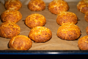 Freshly baked cheese buns cooling on parchment paper. The buns have a golden-brown crust, indicating perfect baking. Ideal for illustrating homemade baking or culinary delights.
