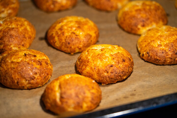 Freshly baked cheese buns cooling on parchment paper. The buns have a golden-brown crust, indicating perfect baking. Ideal for illustrating homemade baking or culinary delights.
