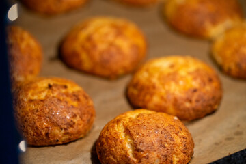 Freshly baked cheese buns cooling on parchment paper. The buns have a golden-brown crust, indicating perfect baking. Ideal for illustrating homemade baking or culinary delights.
