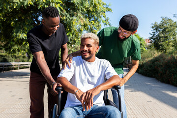 Fototapeta premium Young disabled Black man in a wheelchair and his male friends laughing together in park.