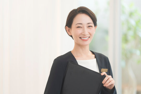 コンシェルジュ。ジャケットを着て黒いファイルを持つ笑顔の日本人女性。
