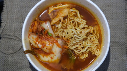 Bowl of Korean ramen noodles in rich red broth, served with kimchi, tofu, and vegetables for a flavorful, spicy comfort meal.