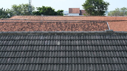 View of overlapping rooftops featuring dark gray concrete tiles in the foreground and orange ceramic tiles in the background.
