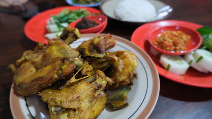 Traditional Indonesian fried chicken served with chili sambal, steamed rice, fresh vegetables, and condiments on colorful plates.
