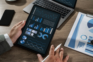 Businessman analyzing financial data and statistics on digital tablet with charts and graphs, concept of analytics, big data, business intelligence, and financial technology.