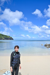 ウエットスーツで南国の海辺に立つ女性のイメージ写真