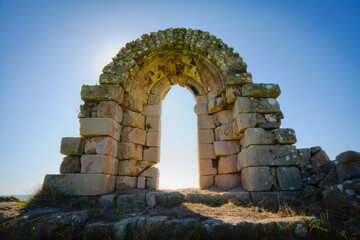 Fototapeta premium Stone archway against a bright blue sky with sunlight shining through the opening in the structure