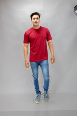 Young man wearing a red t-shirt, denim jeans, and sneakers posing casually in a studio against a plain white background. Ideal for themes of fashion, confidence, and modern lifestyle.