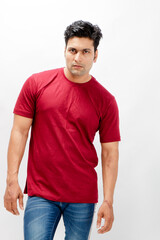 Young man wearing a red t-shirt, denim jeans, and sneakers posing casually in a studio against a plain white background. Ideal for themes of fashion, confidence, and modern lifestyle.