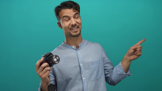 Young hispanic man holding camera pointing at something on isolated green background suggesting idea or direction