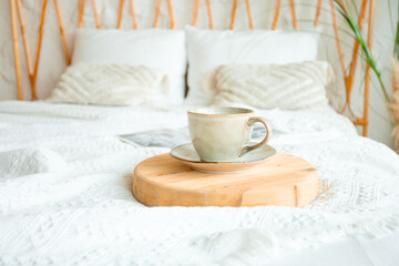 A cup of coffee on a wooden stand, a snow-white bedspread, soft pillows and warm light create an atmosphere of morning peace and harmony.