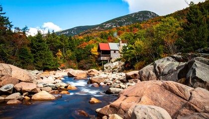A rustic wooden building sits amidst autumn foliage, overlooking a flowing stream surrounded by large rocks.