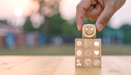 A hand carefully places a wooden block featuring a happy face symbol on top of a stack of blocks with various icons, conveying a sense of growth, happiness, and success.