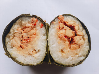 Lemper is served wrapped in green banana leaves on an isolated white background. Lemper is a snack made from sticky rice and cooked