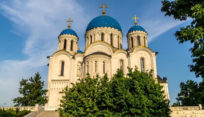 Fototapeta premium A grand cathedral with intricate details and stunning blue domes stands tall against a bright blue sky, framed by lush greenery.