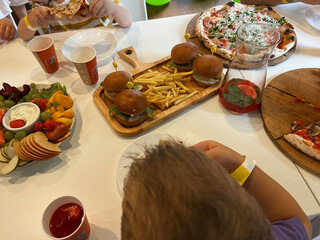 Kids eating pizza, burgers and fruit at party table