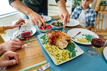 Happy multi-generation family gathering around dining table and having fun during a lunch or dinner on holiday or weekend, food and meat chicken meal closeup