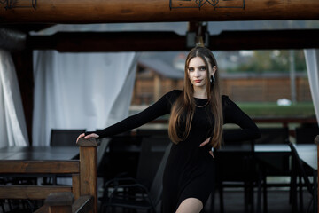 A woman in a black dress with long sleeves stands on a wooden terrace