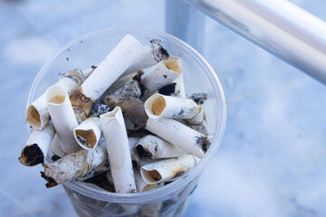 A cup overflowing with discarded cigarette butts on a marble bench