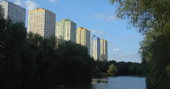 Lake in a beautiful city park on a sunny day. People rent boats and relax going for a row. New high-rise housing complexes are being built in the background.