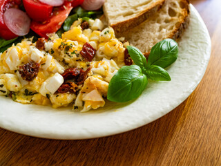 Scrambled eggs with feta cheese and dried tomato, bread and tomato salad on wooden table	
