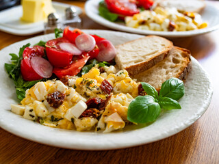 Scrambled eggs with feta cheese and dried tomato, bread and tomato salad on wooden table	
