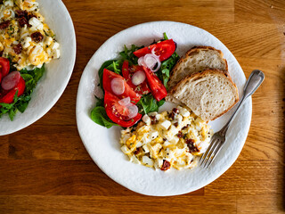 Scrambled eggs with feta cheese and dried tomato, bread and tomato salad on wooden table	