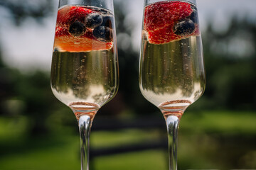 Close-up of two champagne flutes with berries and wedding rings inside, sparkling in natural light — a romantic symbol of celebration and union.