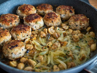 Frying pork meatballs with white mushrooms and onion in frying pan
