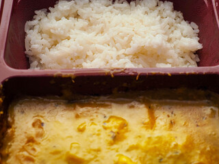 Indian fast food meal with white rice and chicken curry. Close up. Popular dish. Tasty ingredients and spices. Product for heating in microwave. Quick and delicious orient style food.
