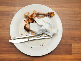 Dirty plate with chicken drumsticks bones and fork and knife on a wooden table. All food is eating. Good appetite concept. Food consumption.