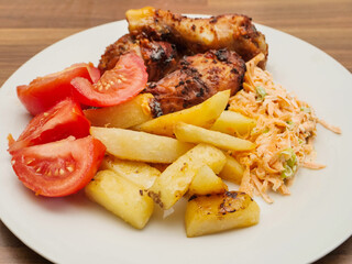 Chicken cooked barbeque marinated drumsticks with chips, tomato and cabbage salad on white plate. Simple taste dinner made of basic products.