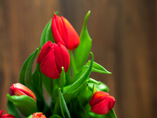 A bouquet of red tulips sits on a wooden table. The flowers are arranged in a vase and are in full bloom, creating a vibrant and cheerful atmosphere. Mothers or valentine day present.