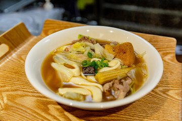 Top-down view of Taiwanese braised tofu with spicy chili broth, garnished with scallions, served in a small white bowl on a wooden tray