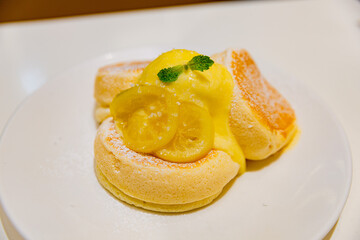 Close-up of soft lemon soufflé pancakes with lemon cream, candied citrus slices, and mint leaf, served on a white plate with powdered sugar