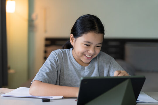 study online class by asian child smile learning on computer tablet or kid girl student fun studying and has dimples on cheeks or young people learn from home school by laptop video call education