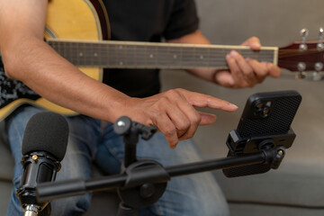 Young man simultaneously playing guitar and recording a podcast at home, illustrating creativity, digital content creation, music, and modern lifestyle