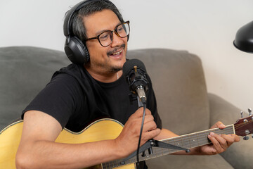 Young man simultaneously playing guitar and recording a podcast at home, illustrating creativity, digital content creation, music, and modern lifestyle