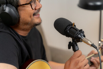 Young man simultaneously playing guitar and recording a podcast at home, illustrating creativity, digital content creation, music, and modern lifestyle
