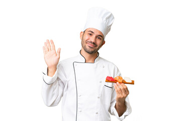 Young caucasian chef holding a sushi over isolated background saluting with hand with happy expression