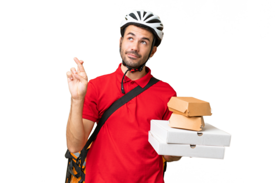 Young handsome caucasian man with thermal backpack and holding takeaway food over isolated background with fingers crossing and wishing the best
