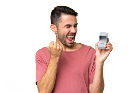 Young handsome caucasian man holding a engagement ring over isolated background celebrating a victory