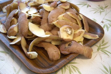 Fresh potato peels on rustic wooden tray prepared for composting, close-up view.