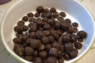 Crispy chocolate cereal balls served with milk in small bowl, nutritious breakfast for children.